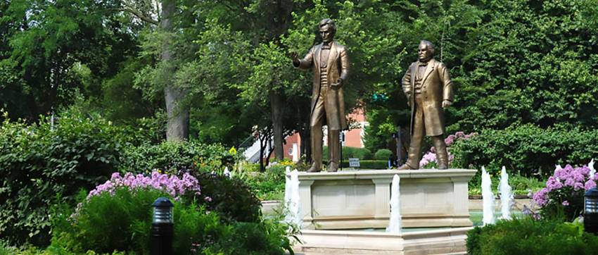 Lincoln and Douglas statues above a fountain surrounded by flowers in Ottawa’s Washington Square.