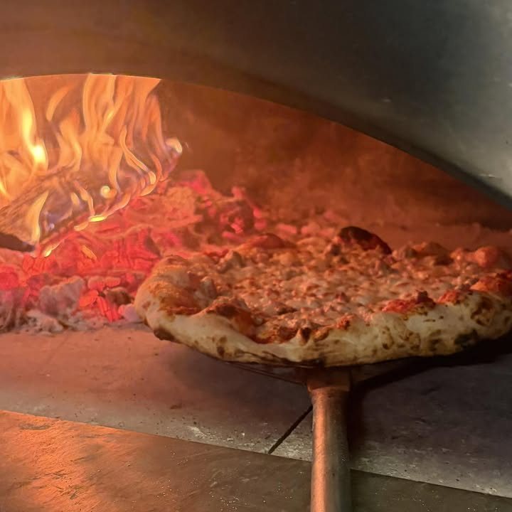 Pizza on a peel beside glowing flames in Sticks and Bricks’ wood-fired oven